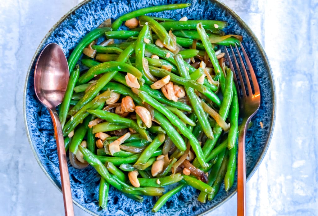 Green Beans with Caramelized Onions & Cashews in a blue bowl with fork and spoon