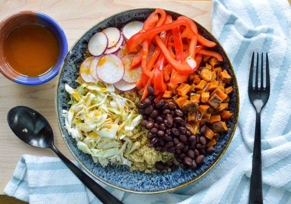 bowl with quinoa, black beans, sweet potatoes, red peppers, radish and cabbage and a chili dressing