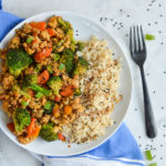 tempeh stir fry with brown rice on a white plate with black fork
